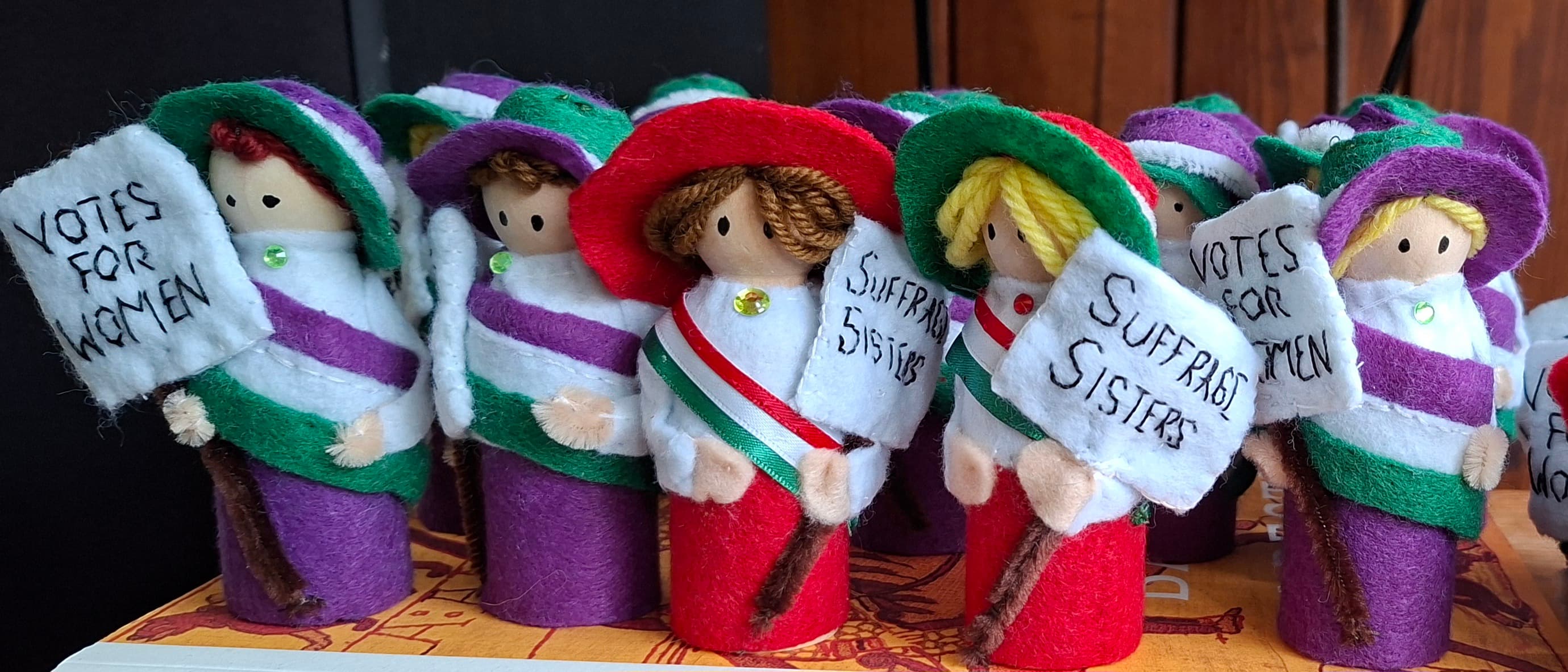 Handmade Suffrage Sisters dolls wearing purple, white and green, holding votes for women banners