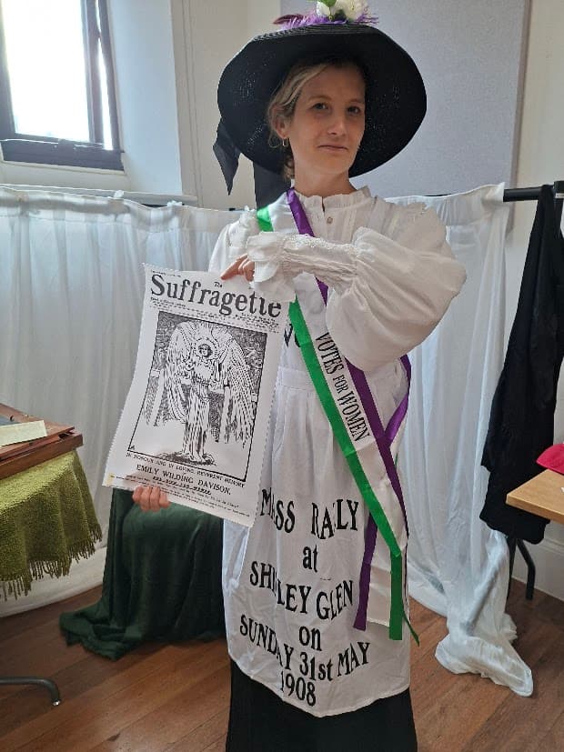 A participant in suffrage dress holding a copy of The Suffragette at the launch